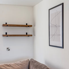 Wooden shelves on a white wall with a framed abstract art piece above a sofa.